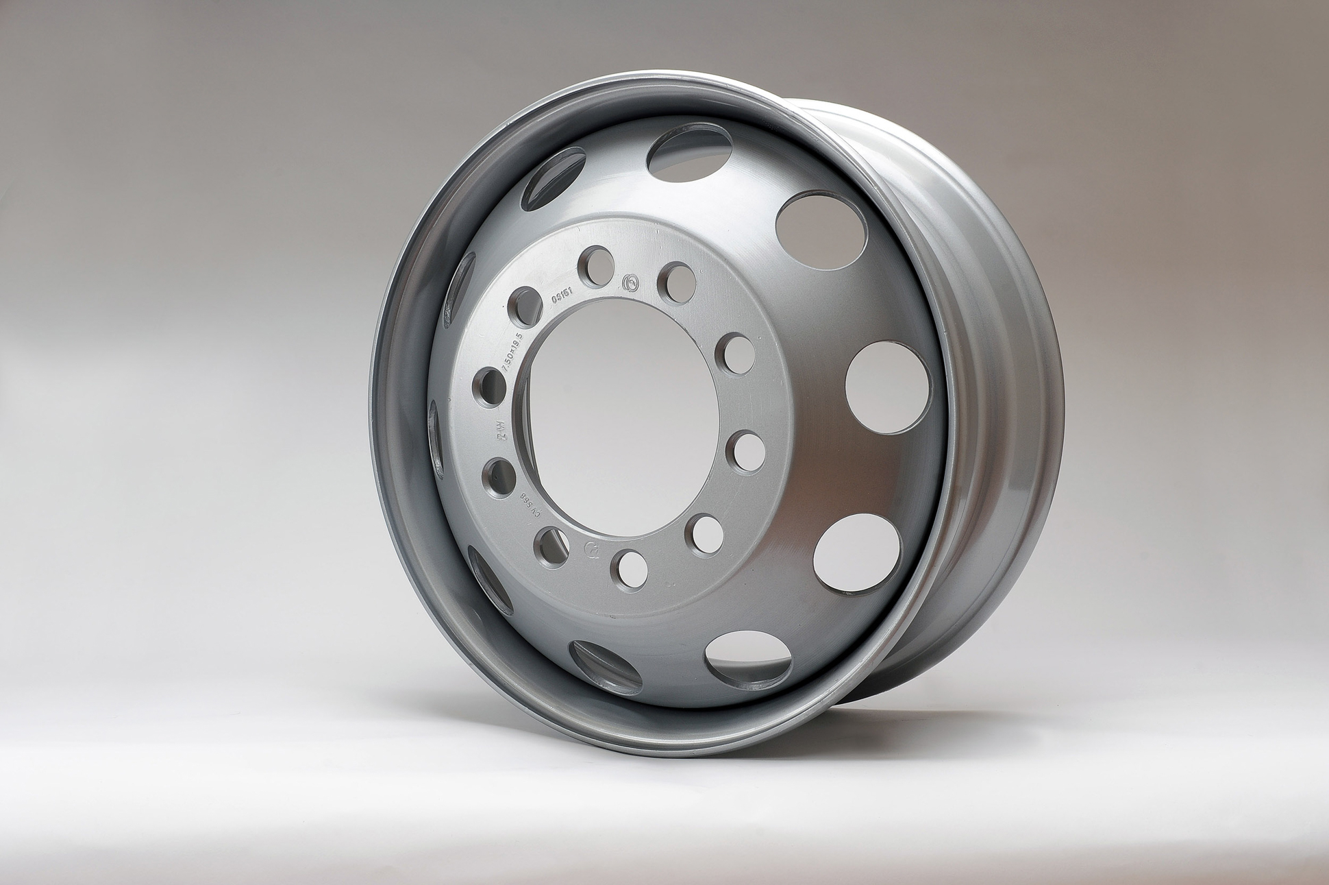 A silver metal wheel rim with multiple round holes is displayed upright against a plain, light background. Steel product manufacturing photography