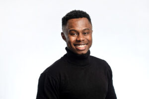 A young man wearing a black turtleneck smiles at the camera against a plain white background, showcasing how to take a professional headshot - taken by Jon Parker Lee Photographer Manchester.