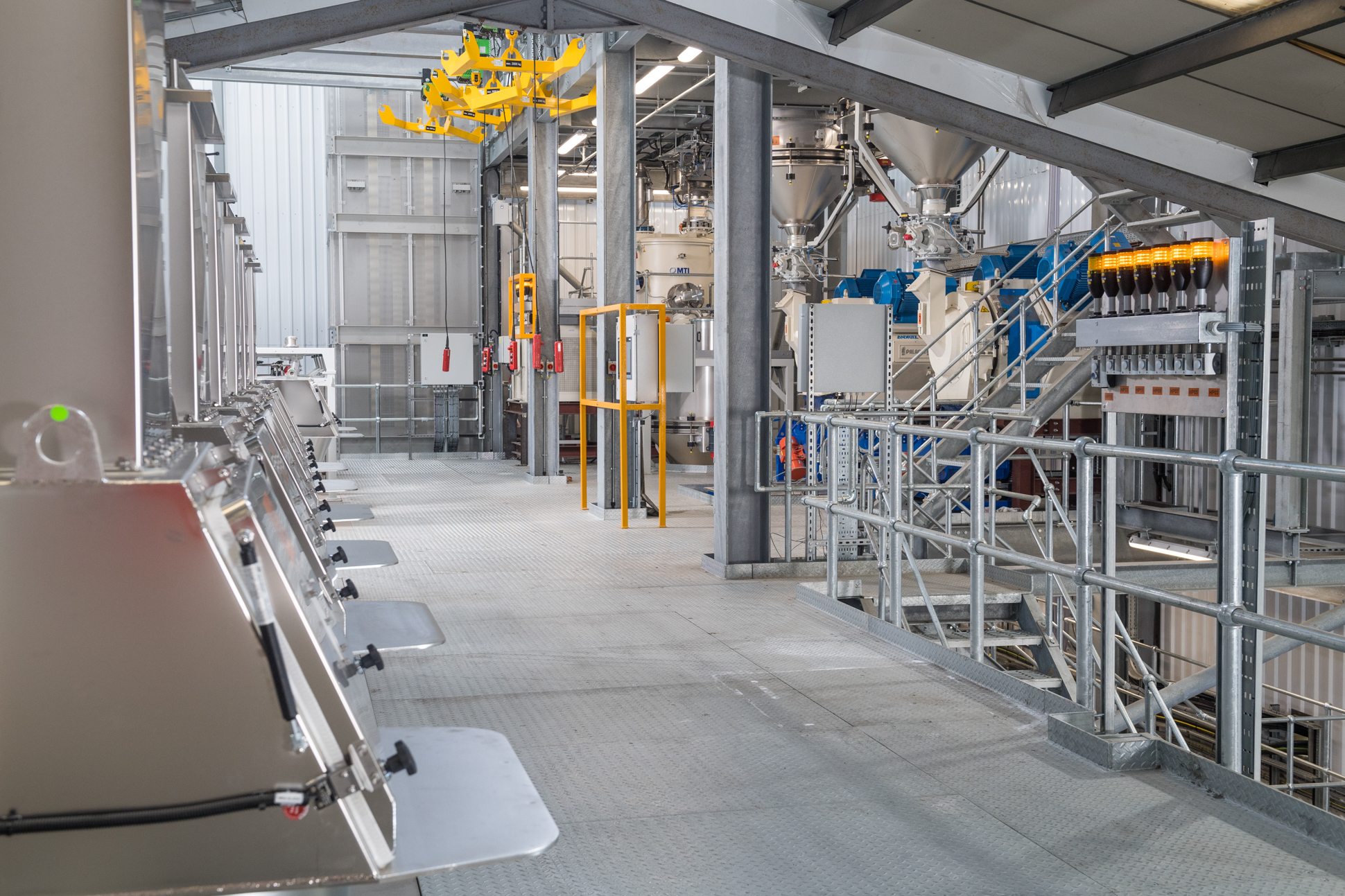 A modern industrial facility with large metal machinery, storage tanks, and pipes, bright lighting, and a clean, organized layout. Overhead rails and platforms are visible, with equipment labeled HP30. Industrial factory equipment photography.